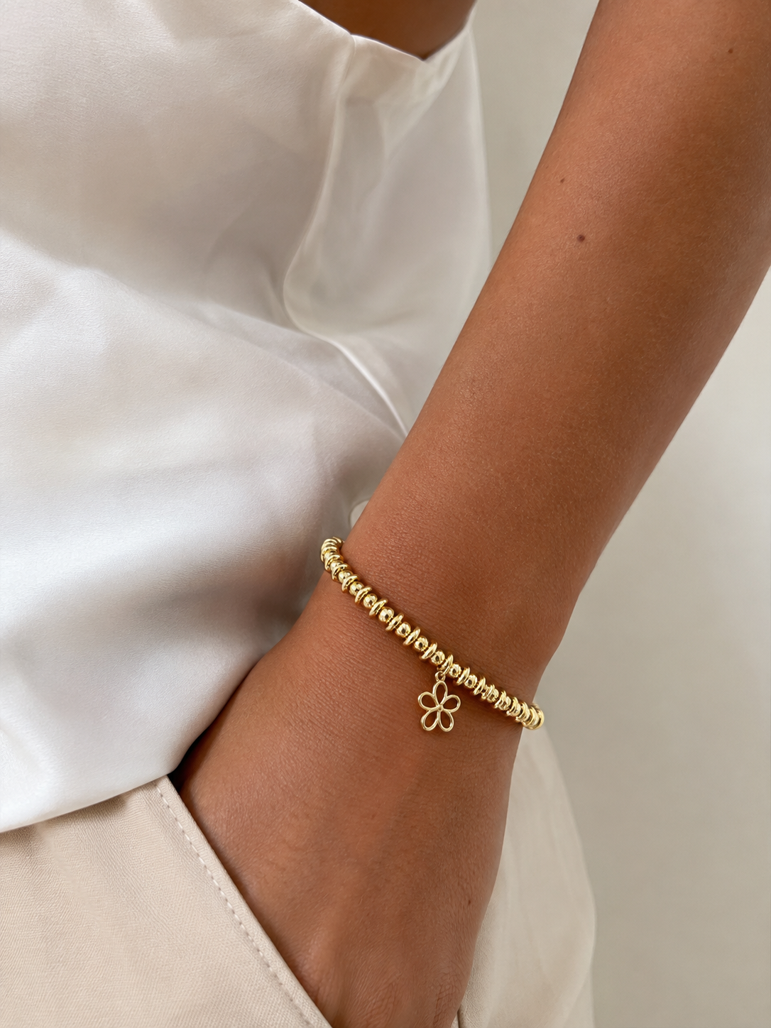 Handgemaakte 18 kt goldfilled armband met gouden kralen en elegant bloemhangertje op witte achtergrond.